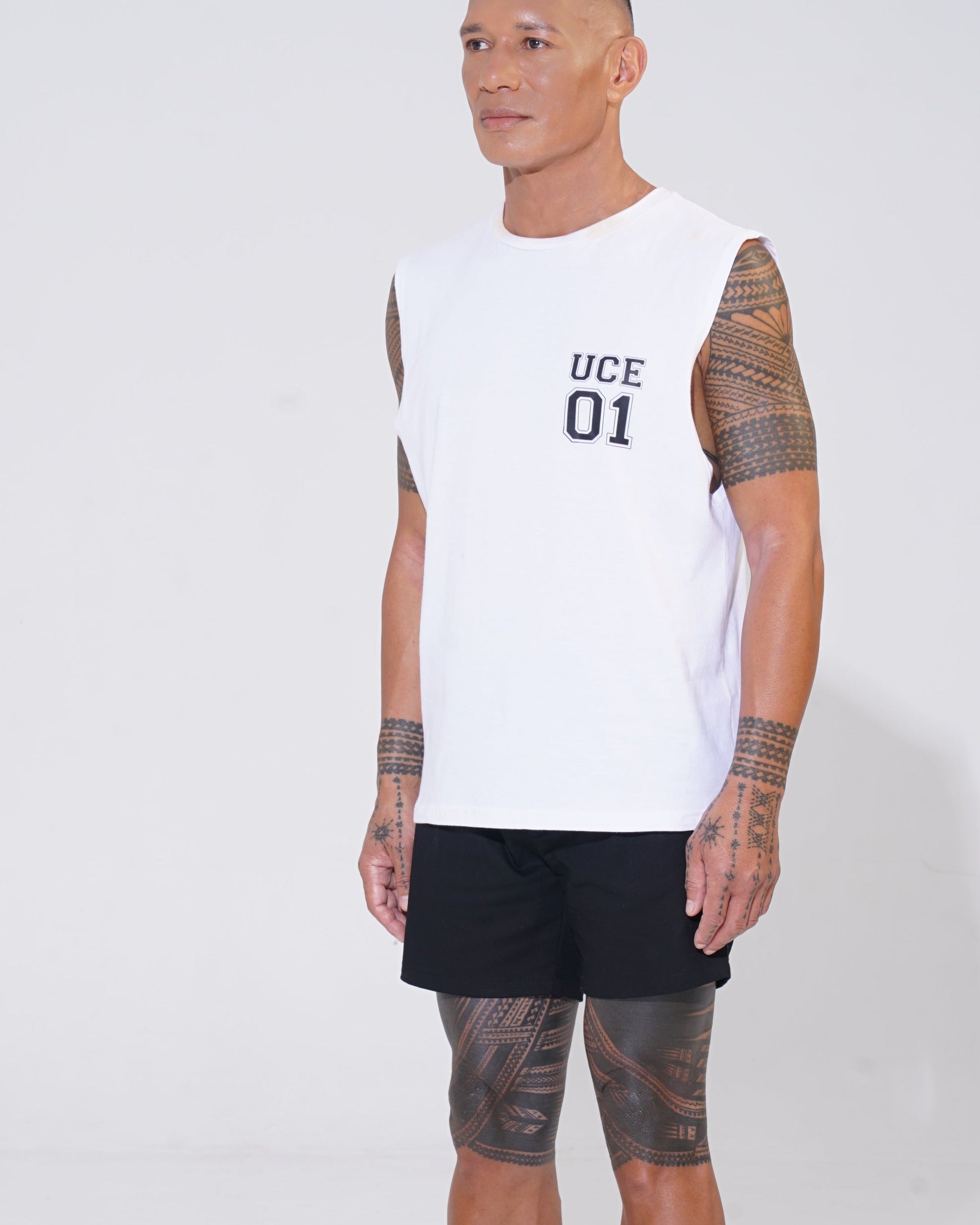Man wearing a white sleeveless shirt with 'UCE 01' text and black shorts on a white background